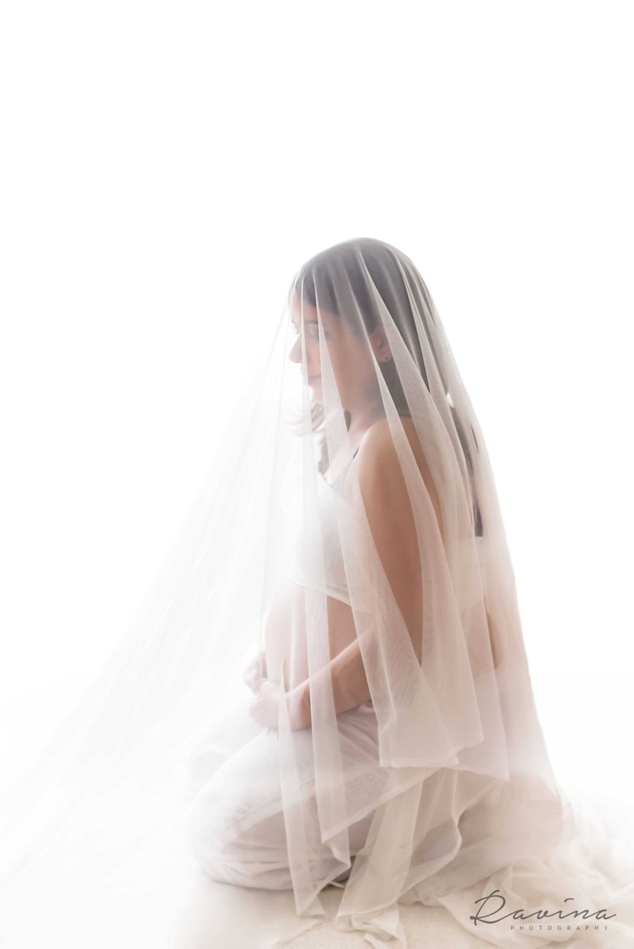 Expectant mother kneeling beneath a sheer white veil, Seattle maternity photography by Ravina Photography